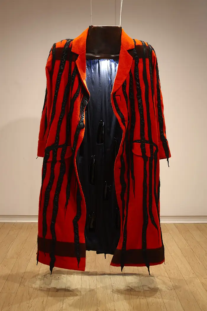 An open red coat with black stripes is hanging from the ceiling. A light inside of it illuminates the lining.