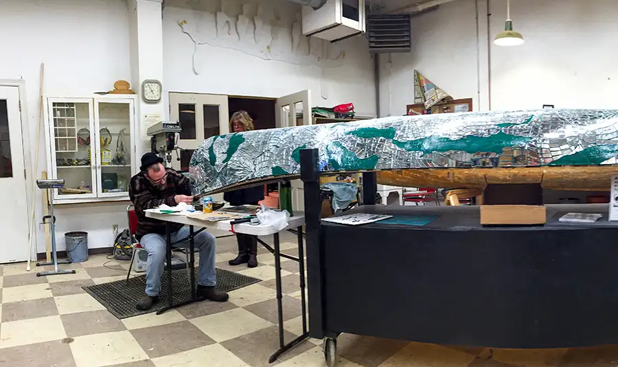 Artist Brad Copping working on a canoe with mirror fragments in a workshop.