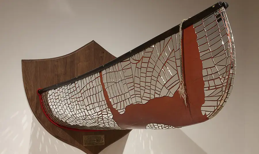 Wooden plaque with half of a canoe with mirror fragments attached to it.