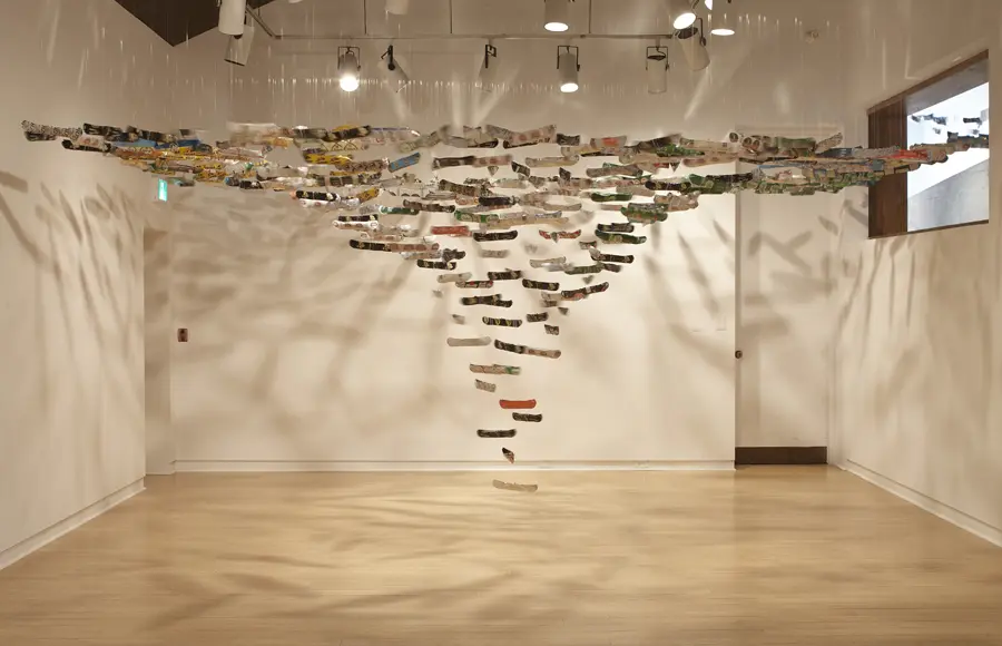 A series of miniature canoe sculptures are hanging from the ceiling in an art gallery.