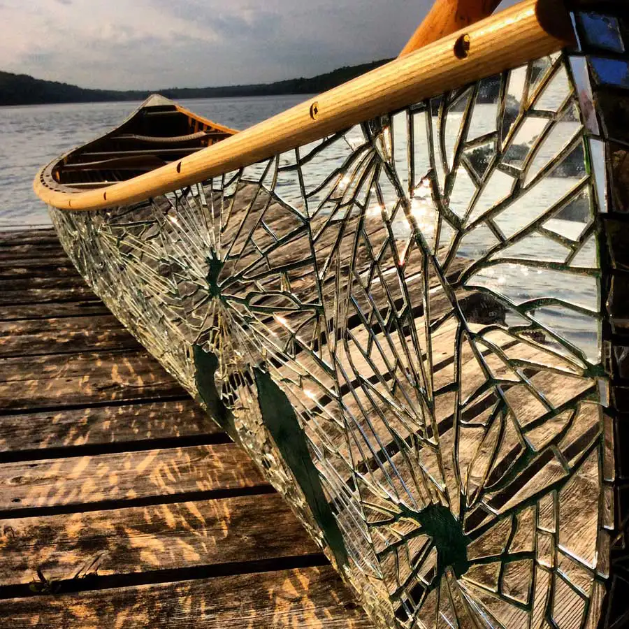 Close up of the end of a canoe with mirror fragments with reflections of a dock and water.