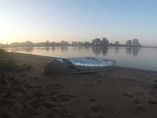 Canoe with mirror fragments is laying on a beach with the bottom facing upwards.