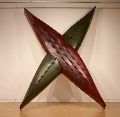 Two canoes, one red, one green, intersect to form an ‘X’ shape. They are leaning against a white wall.