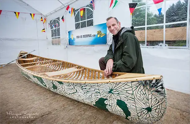 Brad Copping posed beside the mirrored canoe inside a white tent that is decorated with Belgium, Netherlands, United Kingdom, Italian and German flags
