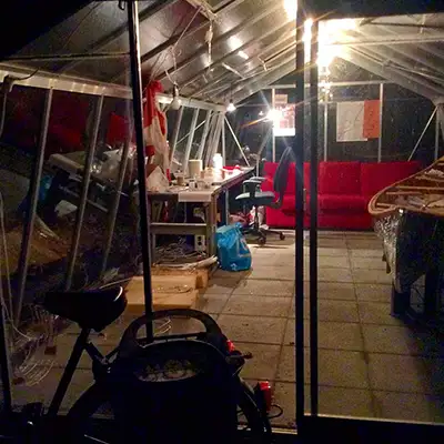 Outside view of a greenhouse with the mirrored canoe, a red couch and a work desk.