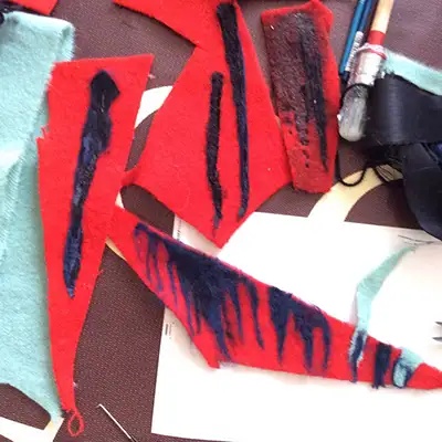 Red and blue fabric with black painted marks beside paintbrushes.