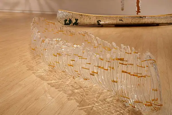 A glass canoe sculpture lying face up on the gallery floor.