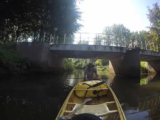 Front shot of artist Brad Copping paddling a canoe under a bridge on a river in Eindhoven.