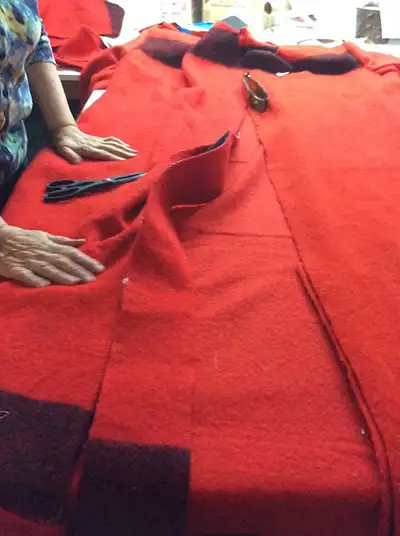 A pair of hands rest on a large sheet of red fabric spread over a table top.