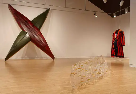 Two canoes, one red and one green, intersect to form an ‘X’ shape. A canoe with glass canoe sculpture lay on the gallery floor on either side.