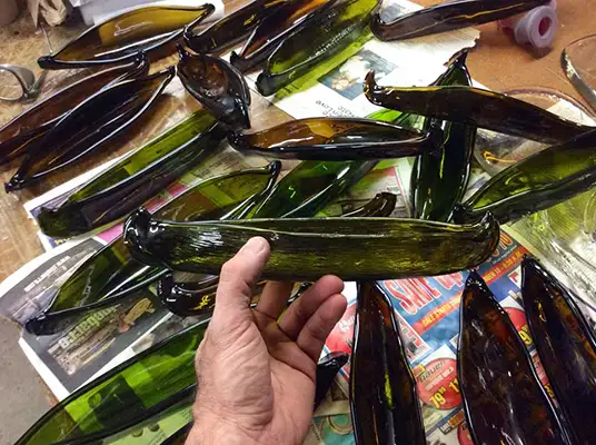 Many miniature green glass canoe sculptures lay on a table with one being held in a persons hand.